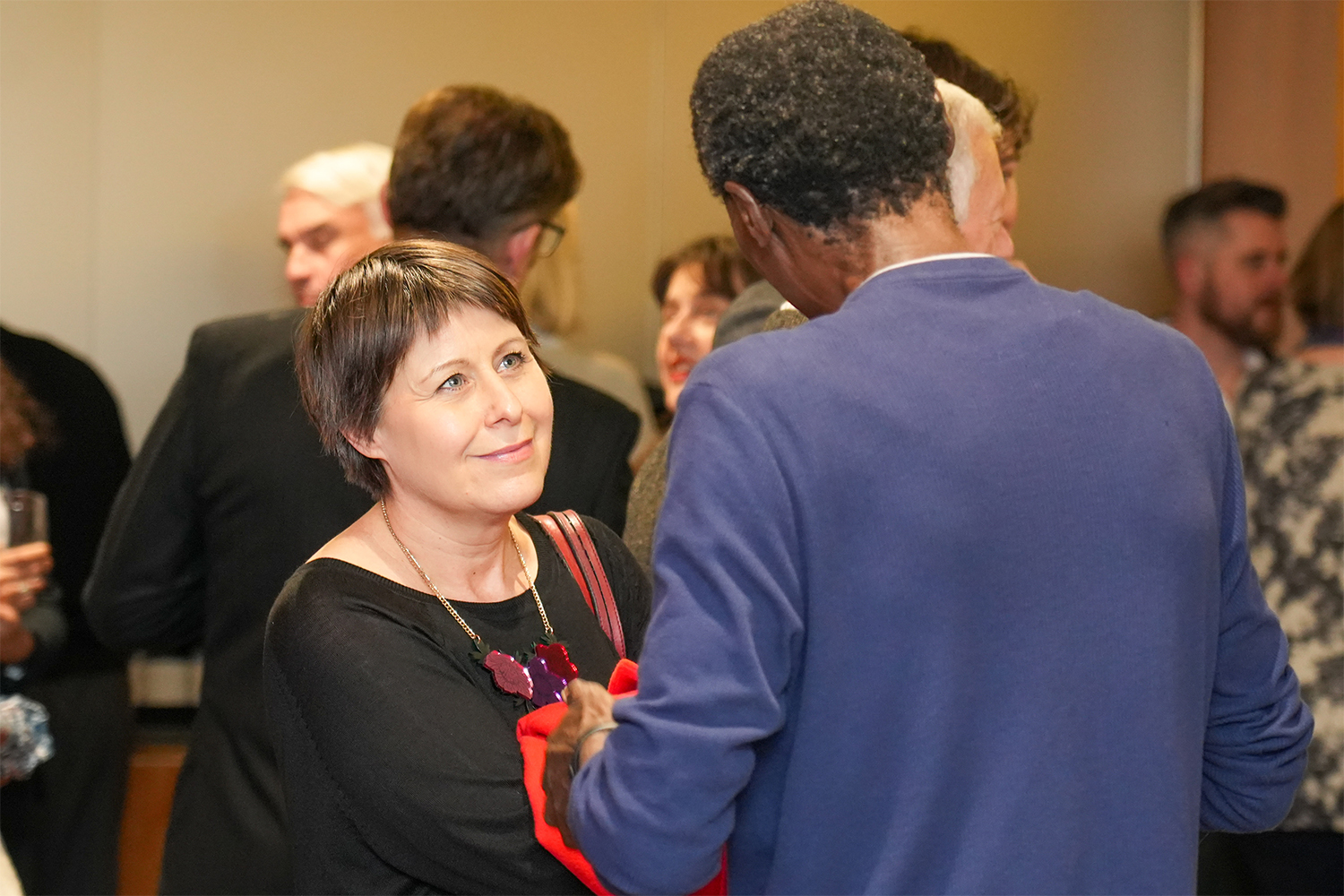 Two chairpersons converse at a networking event, surrounded by additional attendees in the backdrop.